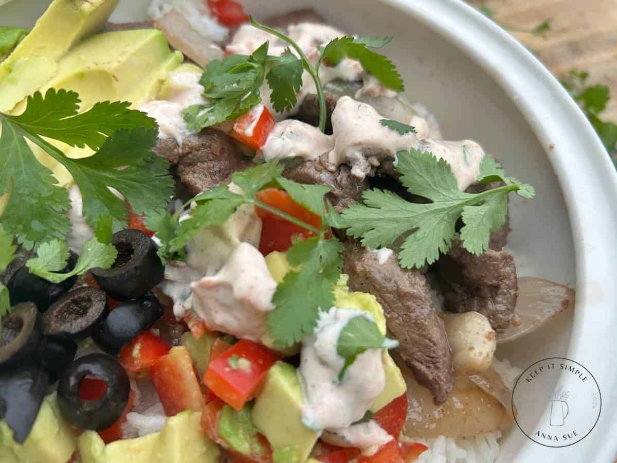 carne-asada-layered-with-rice-venison-streak-carne-asada-sauce-and-cilantro-in-a-white-serving-bowl-up-close-image.jpg