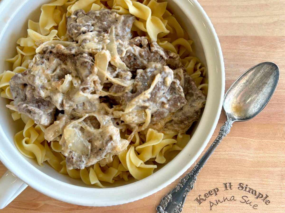 venison-stroganoff-over-wide-egg-noodles-in-a-white-serving-bowl-with-a-vintage-spoon-on-a-cutting-board.jpg