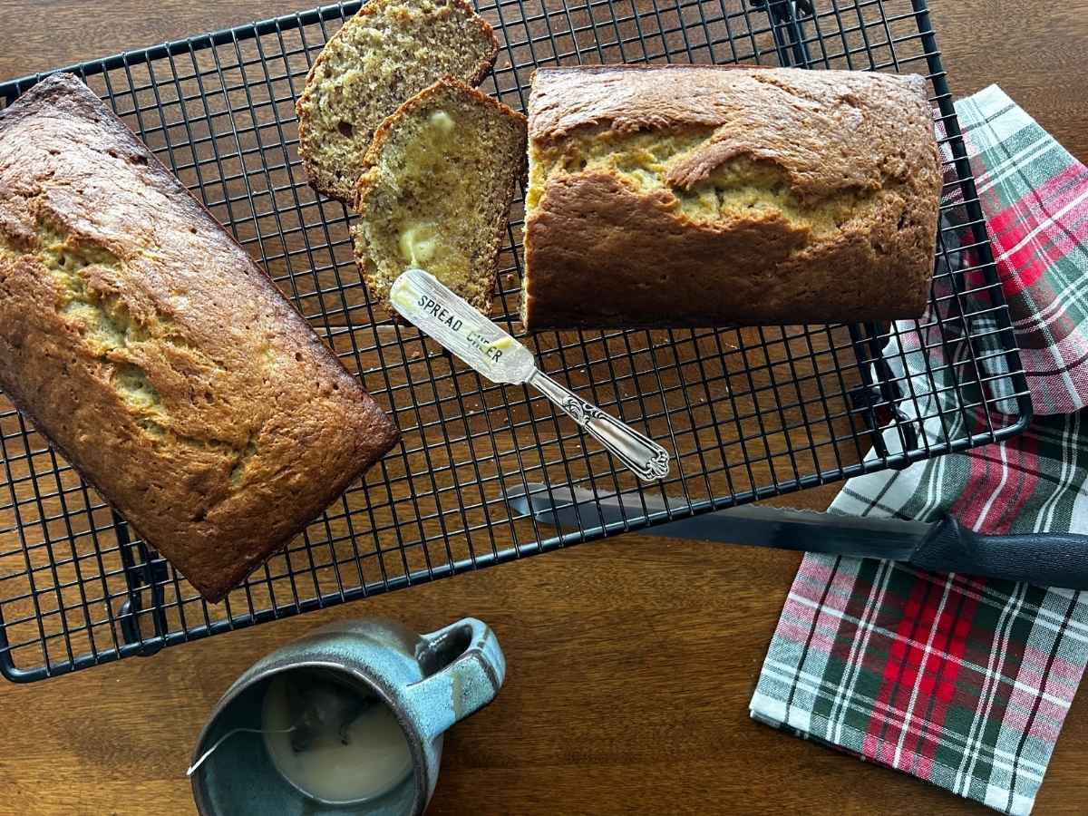 gold medal flour banana bread sliced and buttered one a black cooling rack with a green and red tea towel beside it